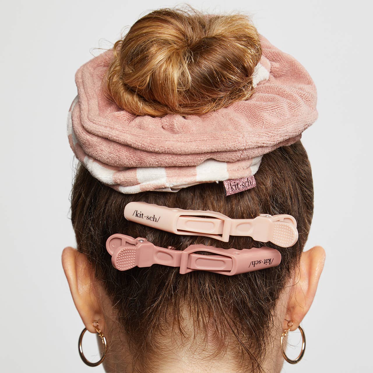 Brown hair in a bun with a pink Microfiber Quick-Dry Towel Scrunchie and two clips, showcasing absorbent, frizz-taming features. Gold hoop earrings visible.
