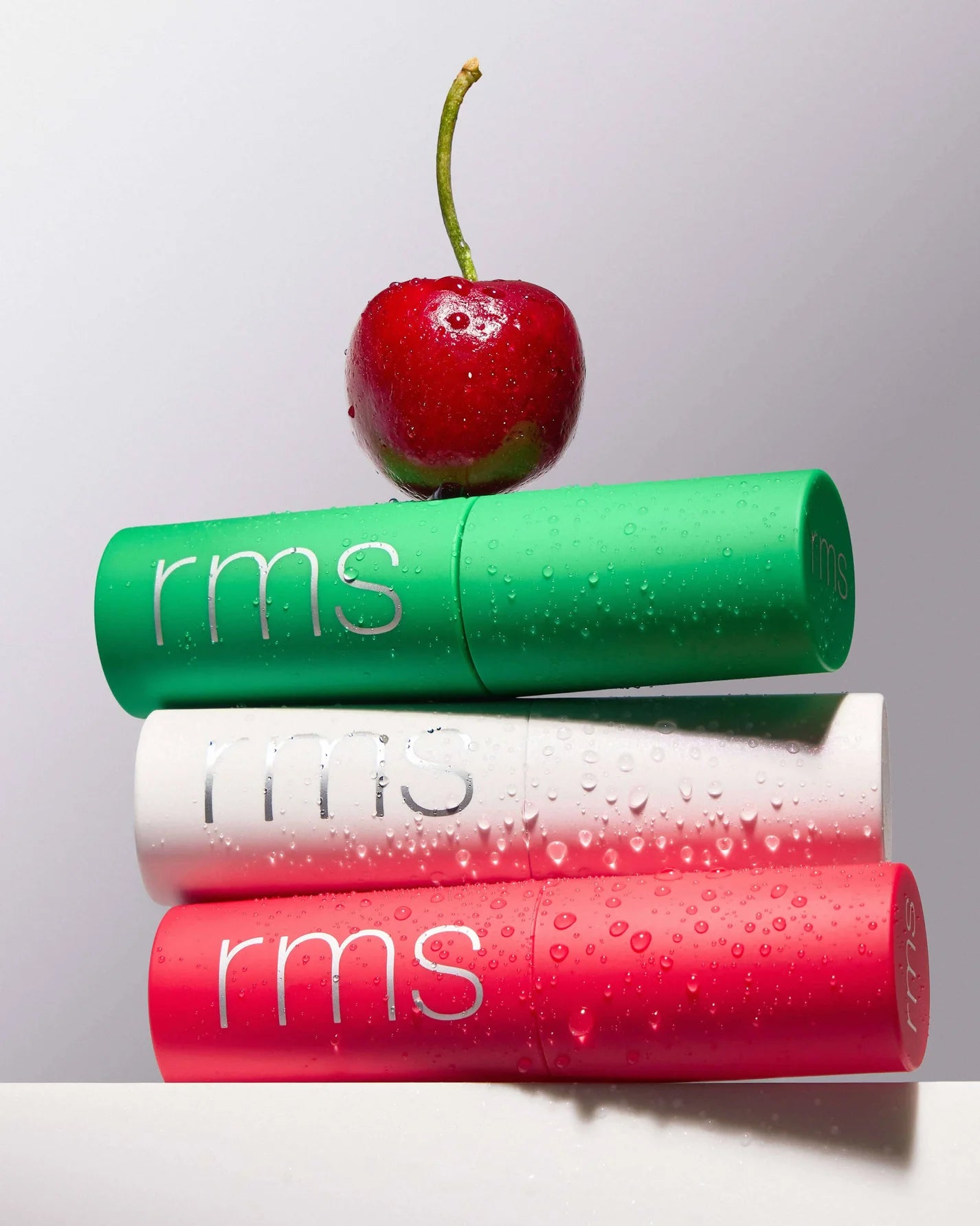 The Mini Lip Oil Trio features three rms branded sticks, topped with a cherry, offering nourishing lip oils in vibrant, personalized shades.