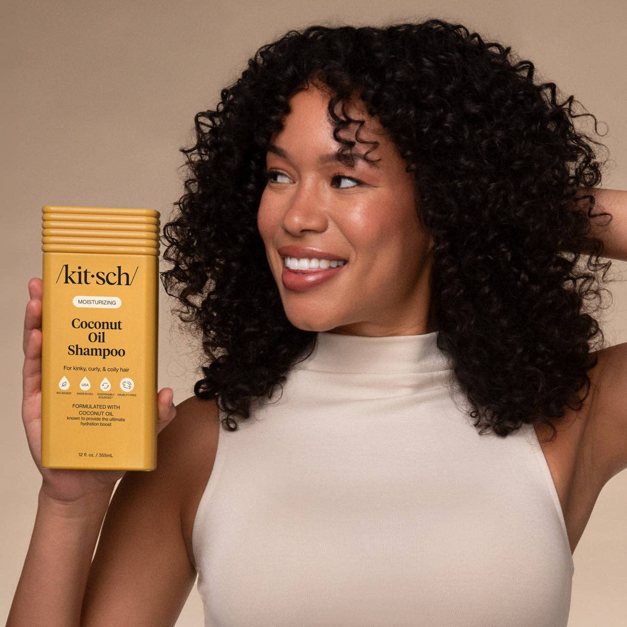Woman holding Kitsch Moisturizing Coconut Oil Shampoo for curly hair, emphasizing hydration and manageability, with eco-friendly packaging from Beauty Shop Bellaire's sustainable haircare line.