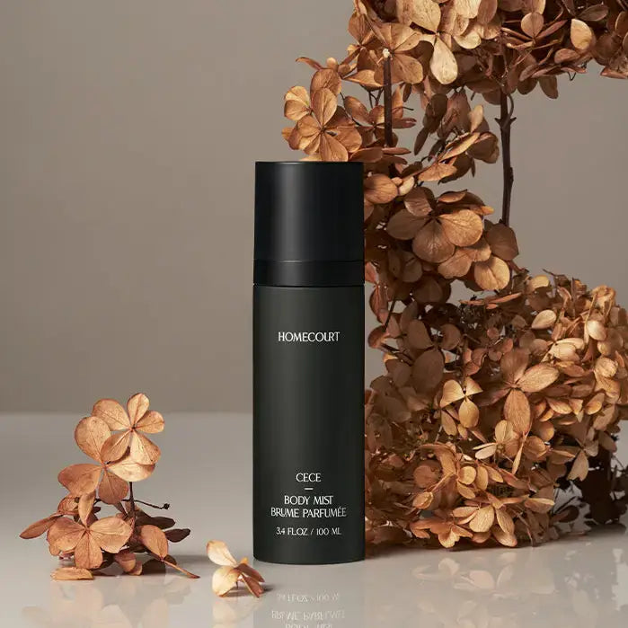 Cece Body Mist | Half Case: Matte-black bottle on glossy surface with dried hydrangeas, featuring a luxurious, sustainable fragrance blend of cedarwood, cardamom, and cinnamon.
