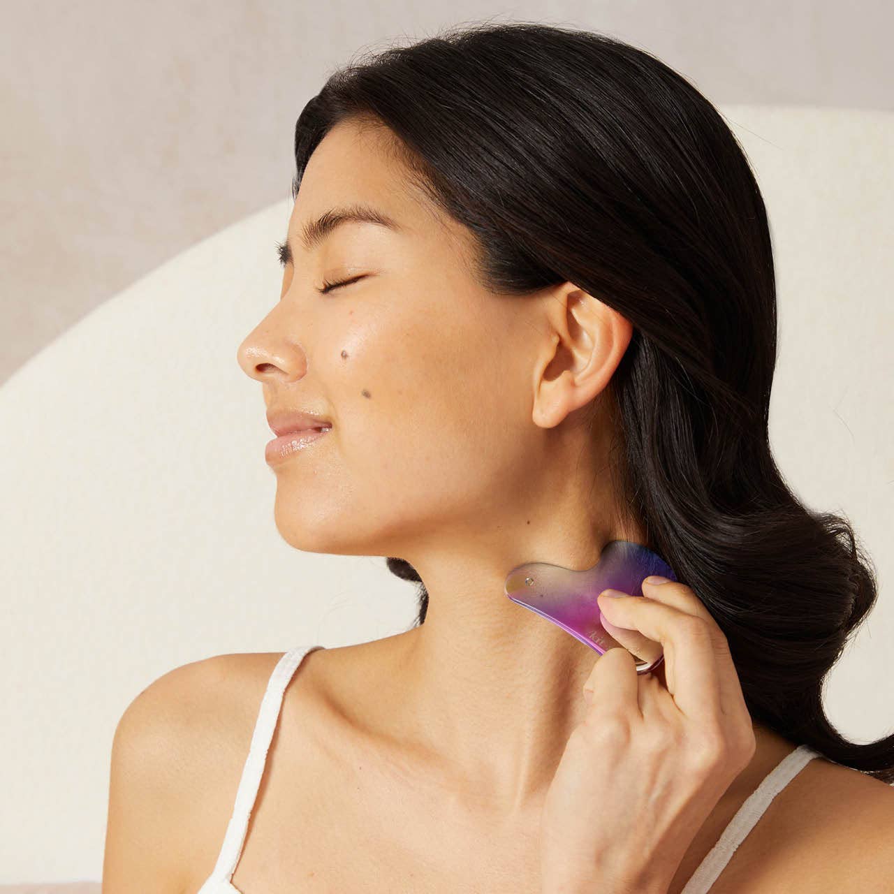 Woman using Kitsch Stainless Steel Gua Sha - Iridescent on neck, eyes closed, enjoying a soothing massage that promotes circulation and relieves tension.