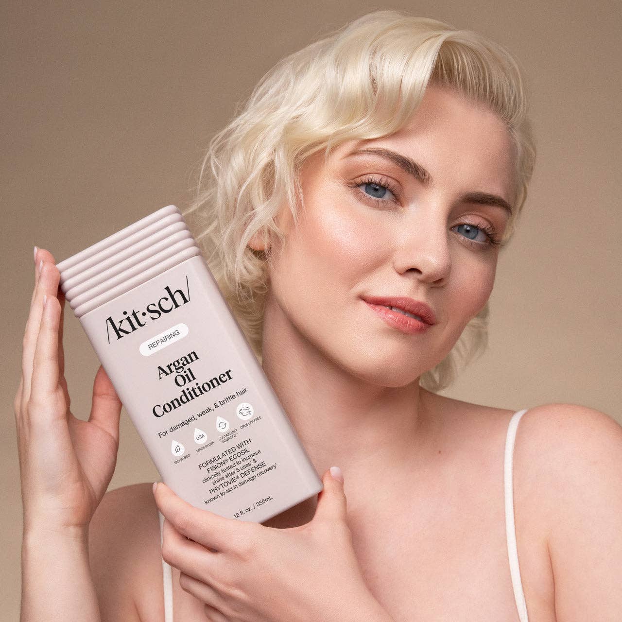 Woman holding Kitsch Repairing Argan Oil Conditioner, highlighting sulfate-free, paraben-free formula for damaged hair, enriched with argan oil and PhytoVie® Defense for shine.