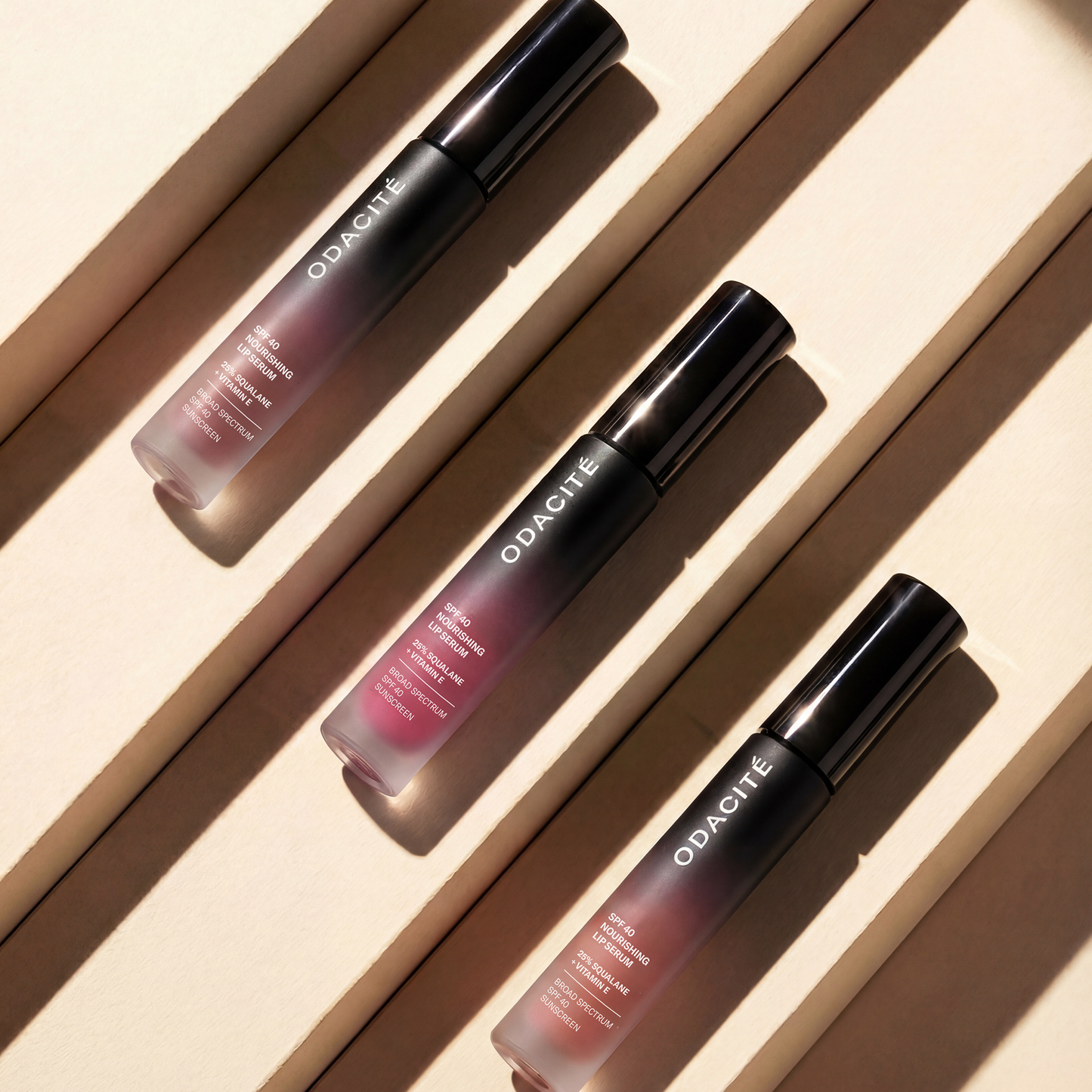 Three Odacité SPF 40 Nourishing Lip Serum tubes arranged on a beige backdrop, highlighting their protective, hydrating formula with squalane and vitamin E.