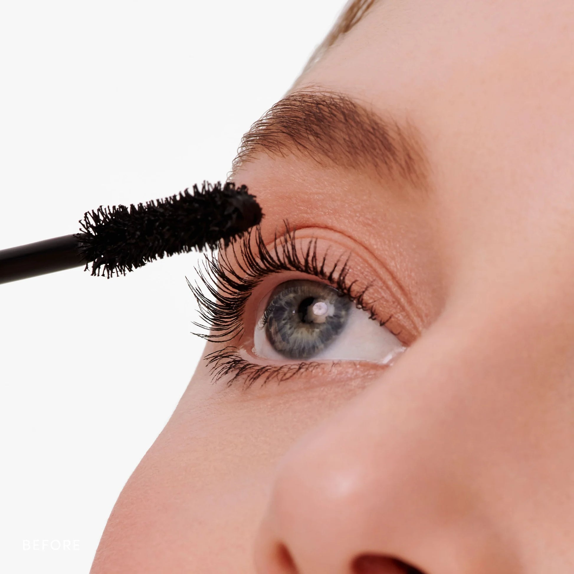 Close-up of an eye with Beyond Lash™ Volumizing Mascara wand enhancing upper lashes, showcasing bold, natural volume and length in a clean, nourishing formula.