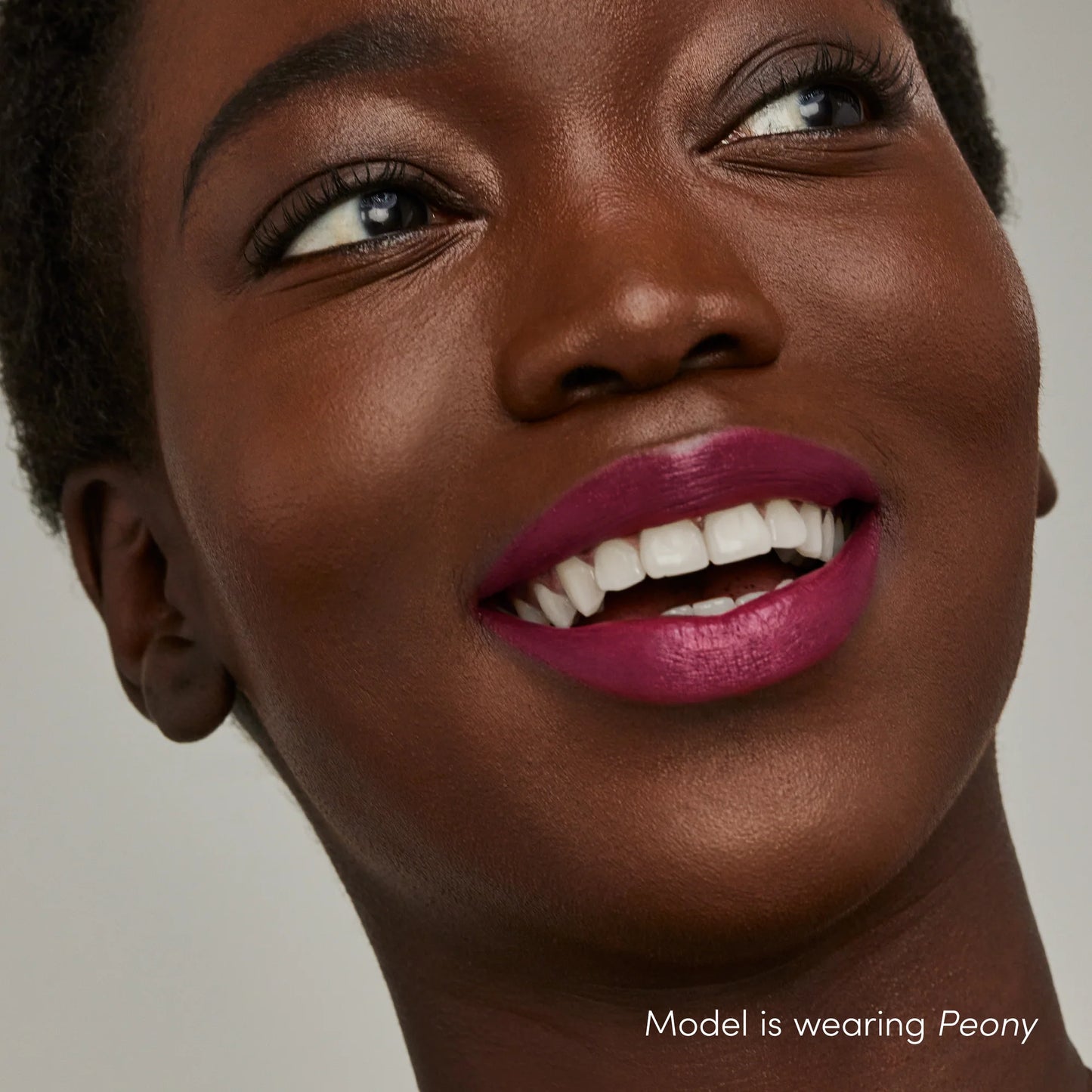 Woman with radiant smile wearing ColorLuxe Hydrating Cream Lipstick in Peony, showcasing its vibrant magenta-pink hue and nourishing, satin finish.