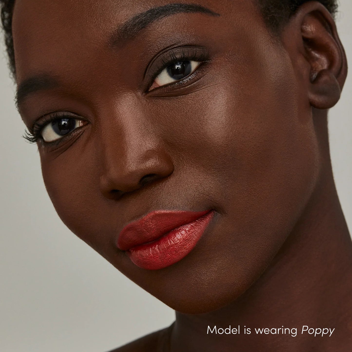 Dark-skinned woman wearing ColorLuxe Hydrating Cream Lipstick in Poppy, showcasing vibrant, creamy color with a satin finish.