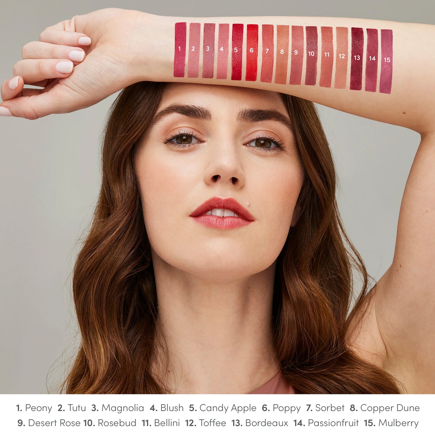 Woman showcasing ColorLuxe Hydrating Cream Lipstick swatches on forearm, featuring 15 shades from Peony to Mulberry, highlighting vibrant, nourishing, and creamy formula.