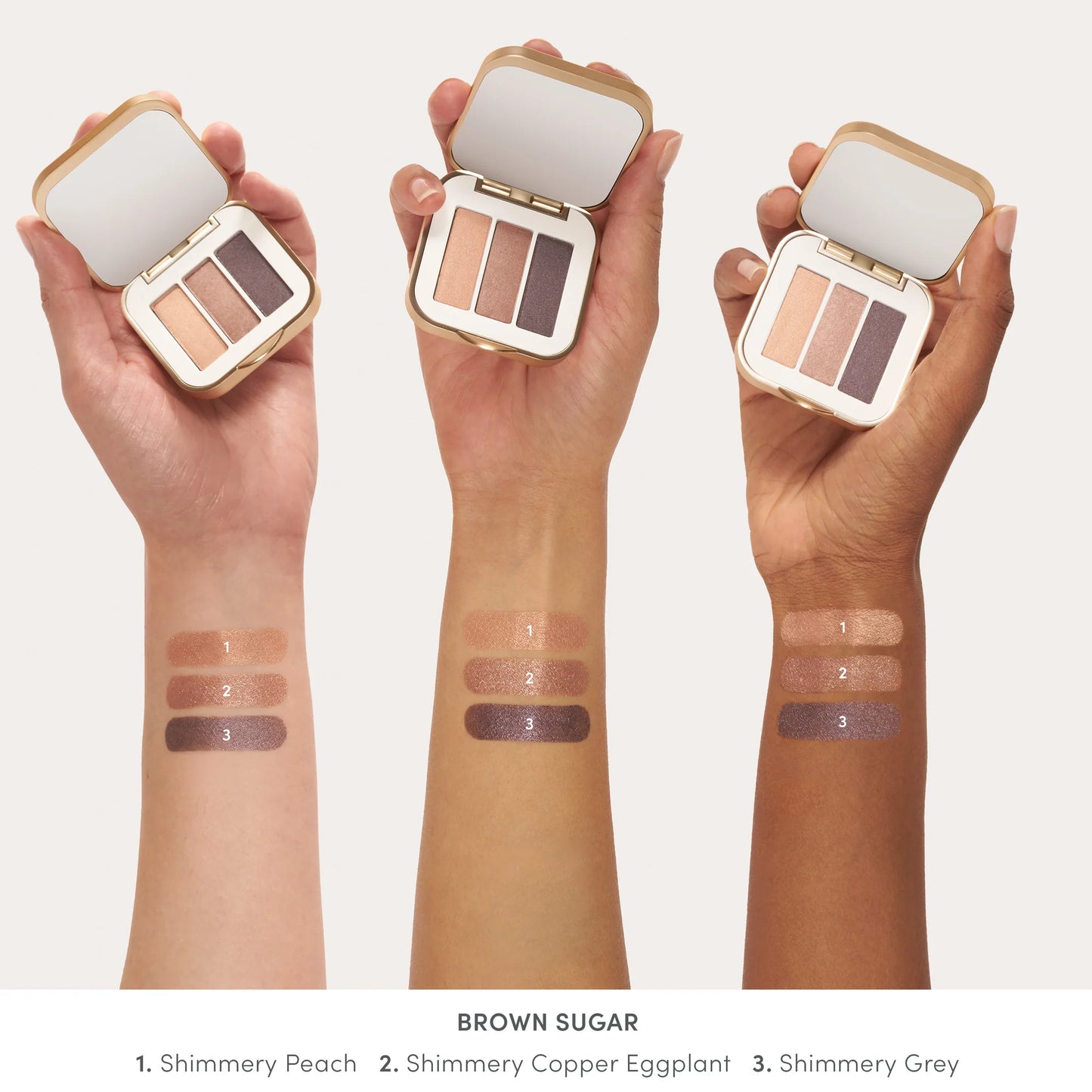 Three diverse hands hold the PurePressed® Eye Shadow Triple, showcasing its three shimmery shades and swatches on light, medium, and deep skin tones.