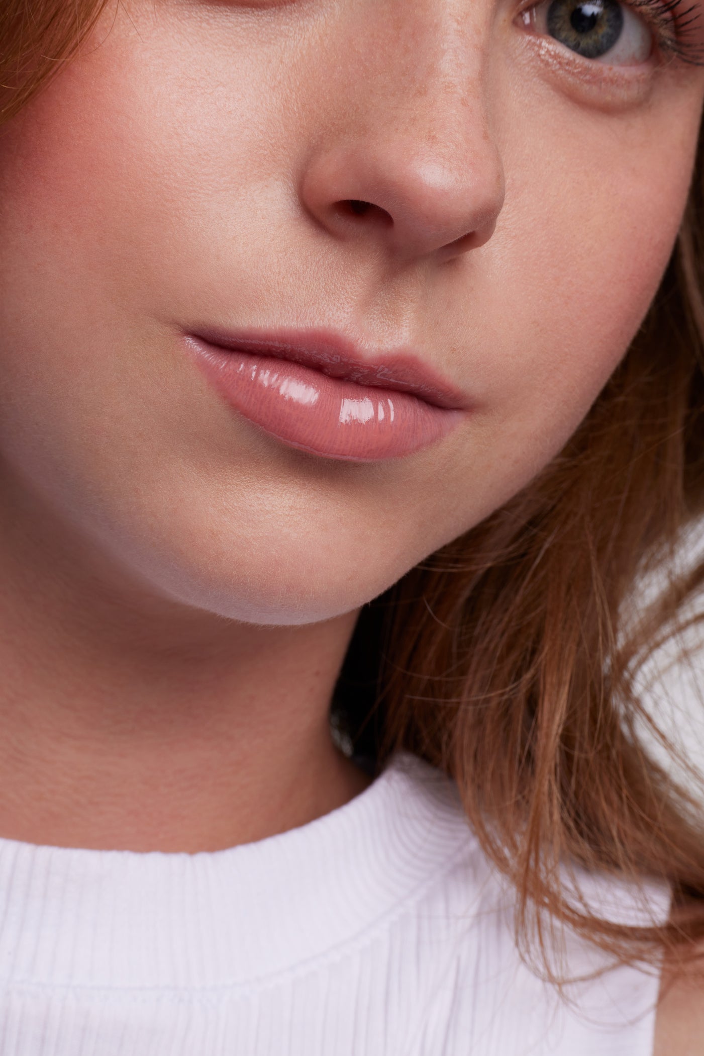 ColorLuxe High Impact Lip Glaze on glossy lips, showcasing smooth, freckled skin, with strands of light brown hair and a ribbed white top visible.