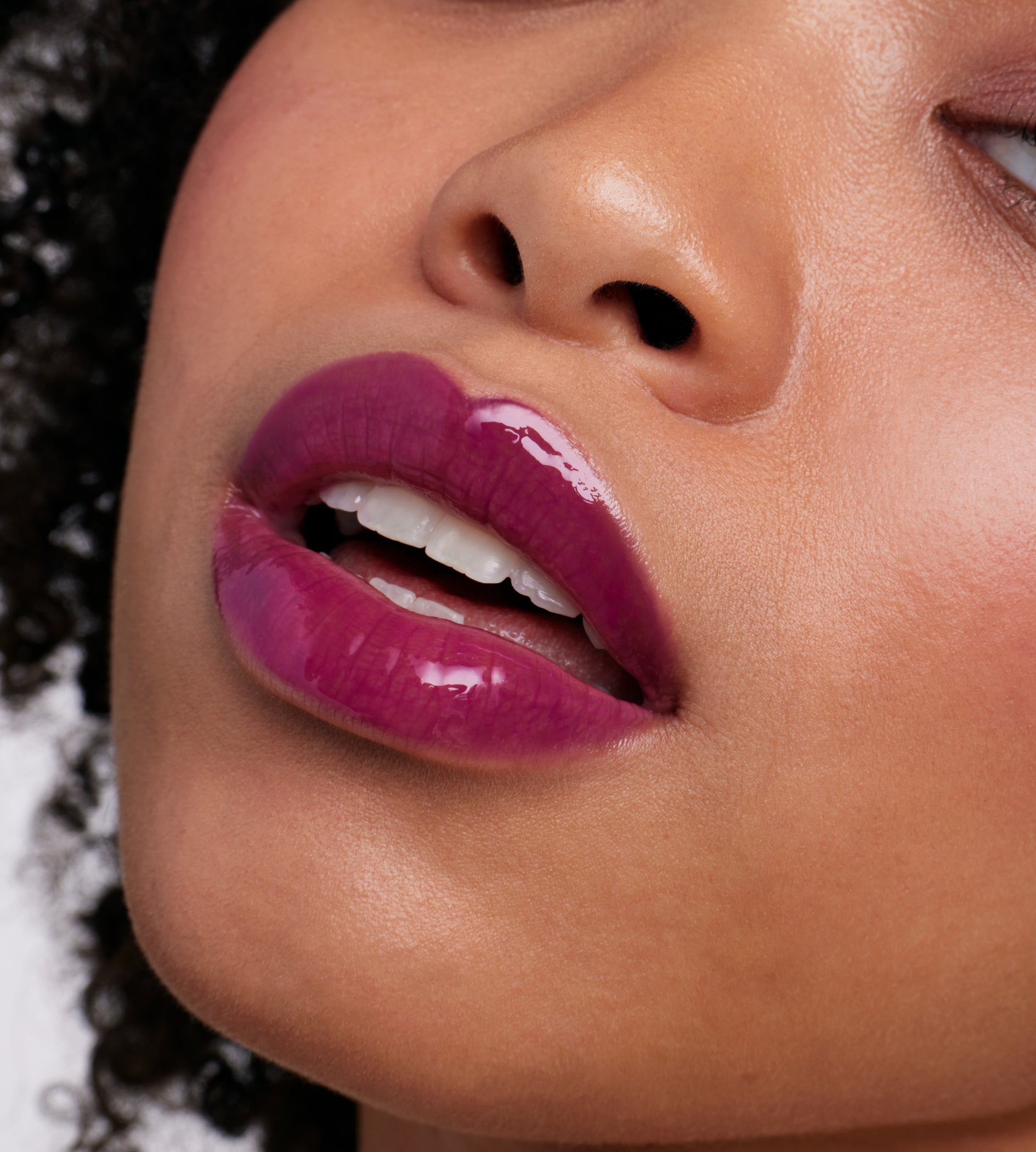 Close-up of lips wearing ColorLuxe High Impact Lip Glaze in deep magenta-purple, showcasing its glossy, bold pigmentation on a medium-brown complexion.