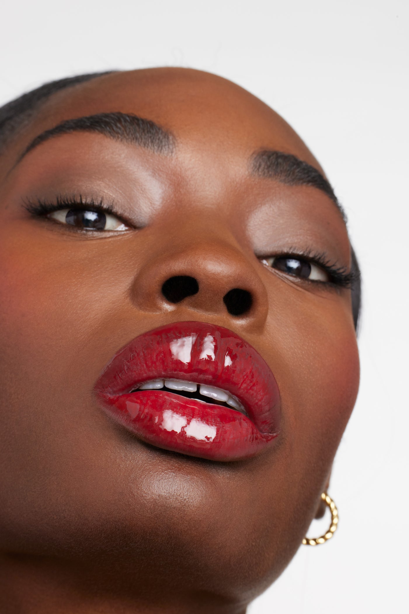 Close-up of glossy, vibrant red lips showcasing ColorLuxe High Impact Lip Glaze's intense pigmentation and shine, complemented by well-groomed brows and subtle eyeshadow.