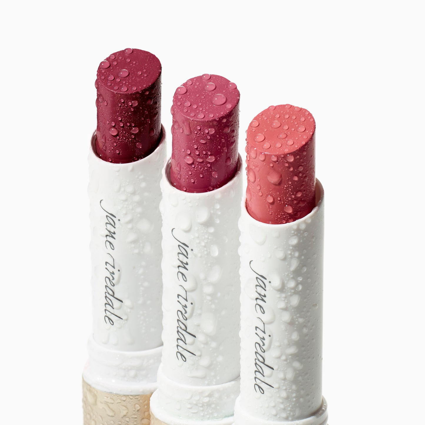 ColorLuxe Hydrating Cream Lipstick in deep berry, rose-pink, and coral, housed in dewy white tubes embossed with “jane iredale” logo, exemplifying vibrant, nourishing color.
