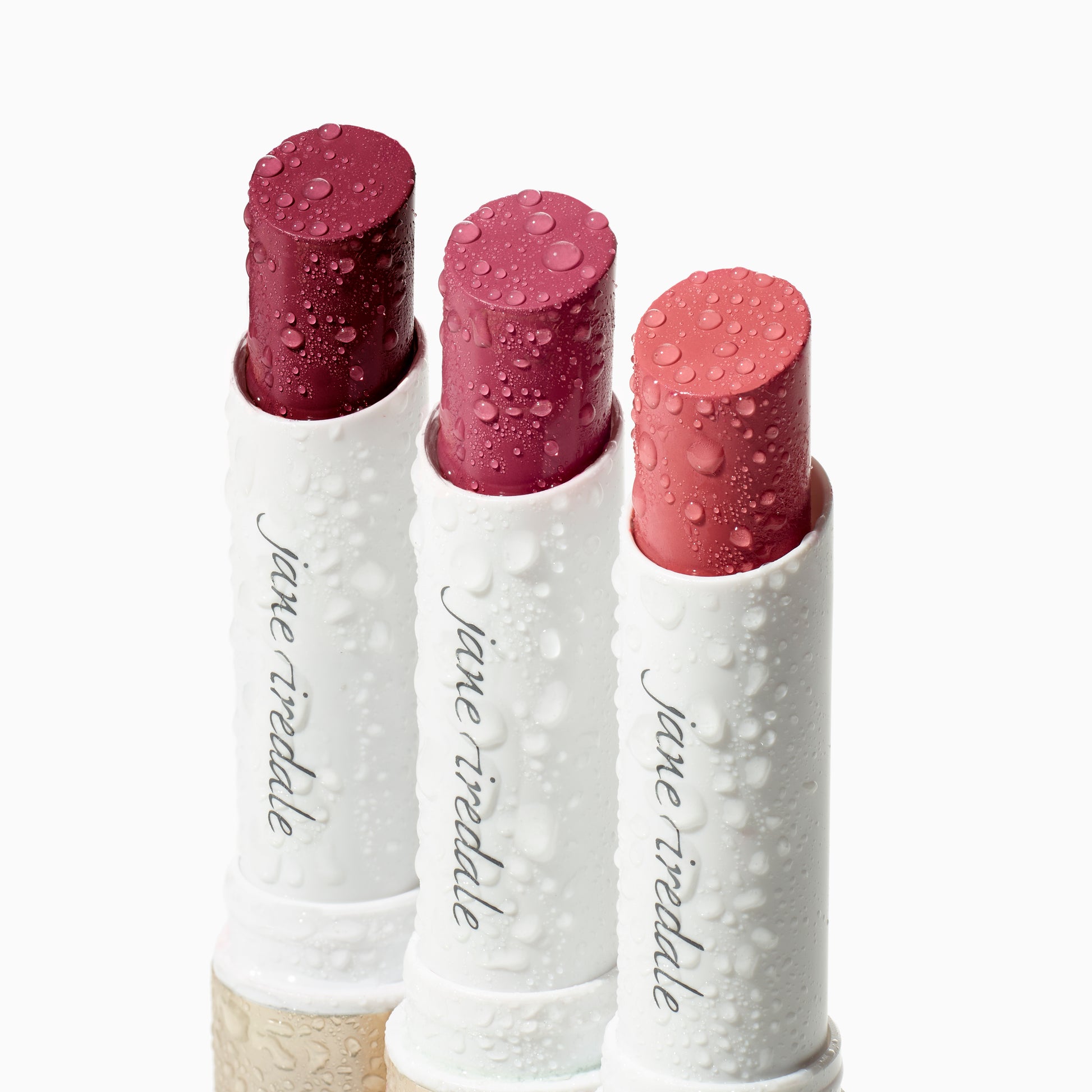 ColorLuxe Hydrating Cream Lipstick in deep berry, rose-pink, and coral, housed in dewy white tubes embossed with “jane iredale” logo, exemplifying vibrant, nourishing color.