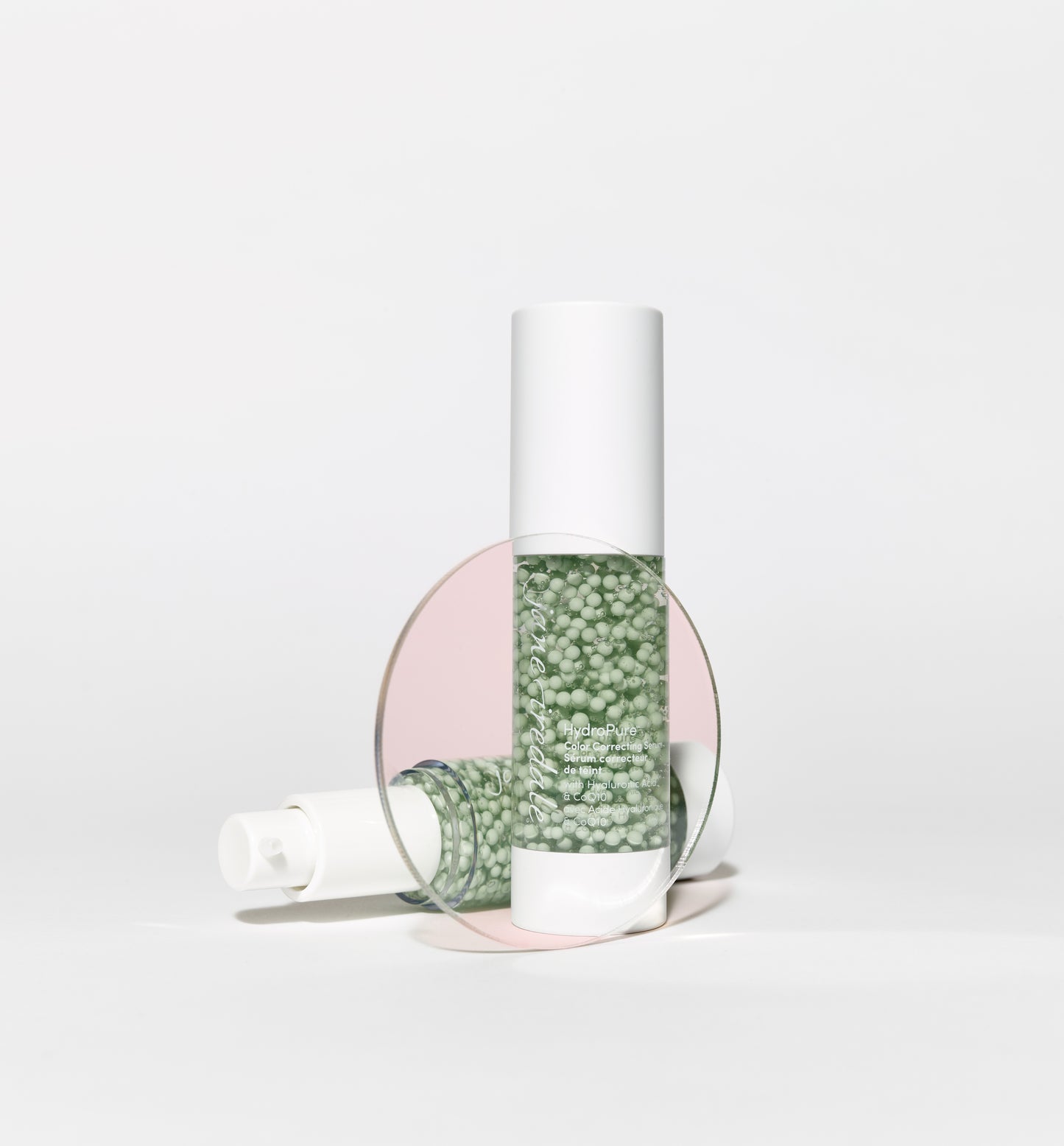 HydroPure™ Color Correcting Serum bottles, one upright, one lying down, feature pale green gel with beads; offers hydration and skin tone correction.