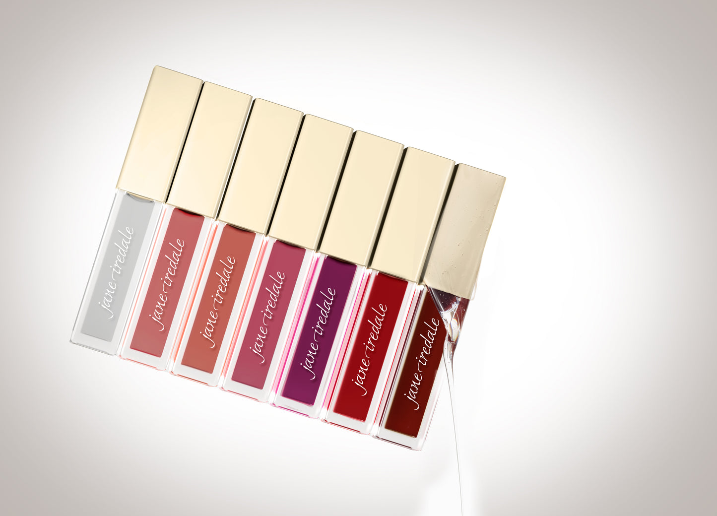 ColorLuxe High Impact Lip Glaze tubes with gold caps, showcasing shades from clear to deep red. The open tube highlights the gloss's rich, nourishing finish.