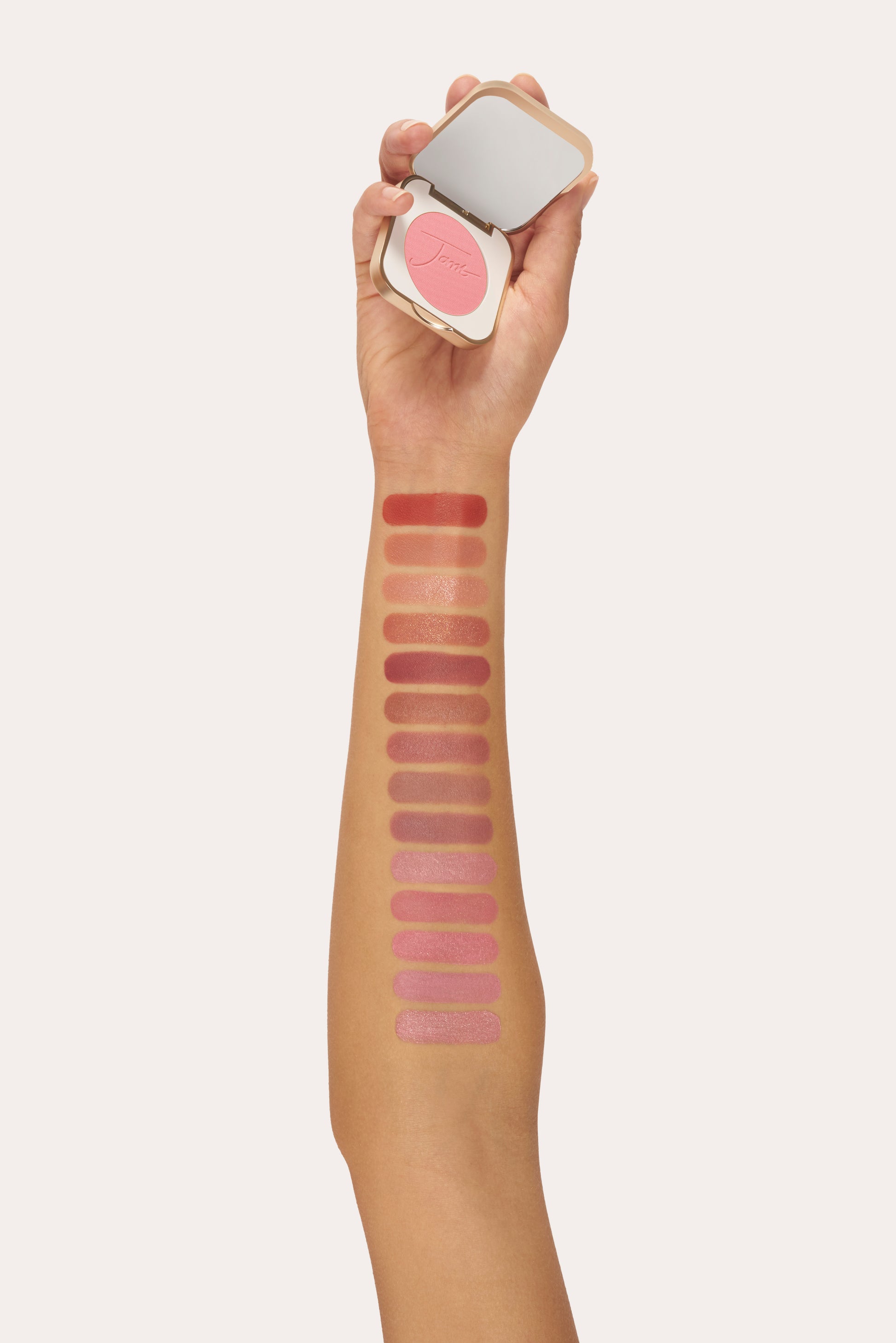 Forearm with swatches of pink-toned makeup; hand holds PurePressed® Blush compact in soft pink, showcasing silky, buildable mineral formula from Beauty Shop Bellaire.