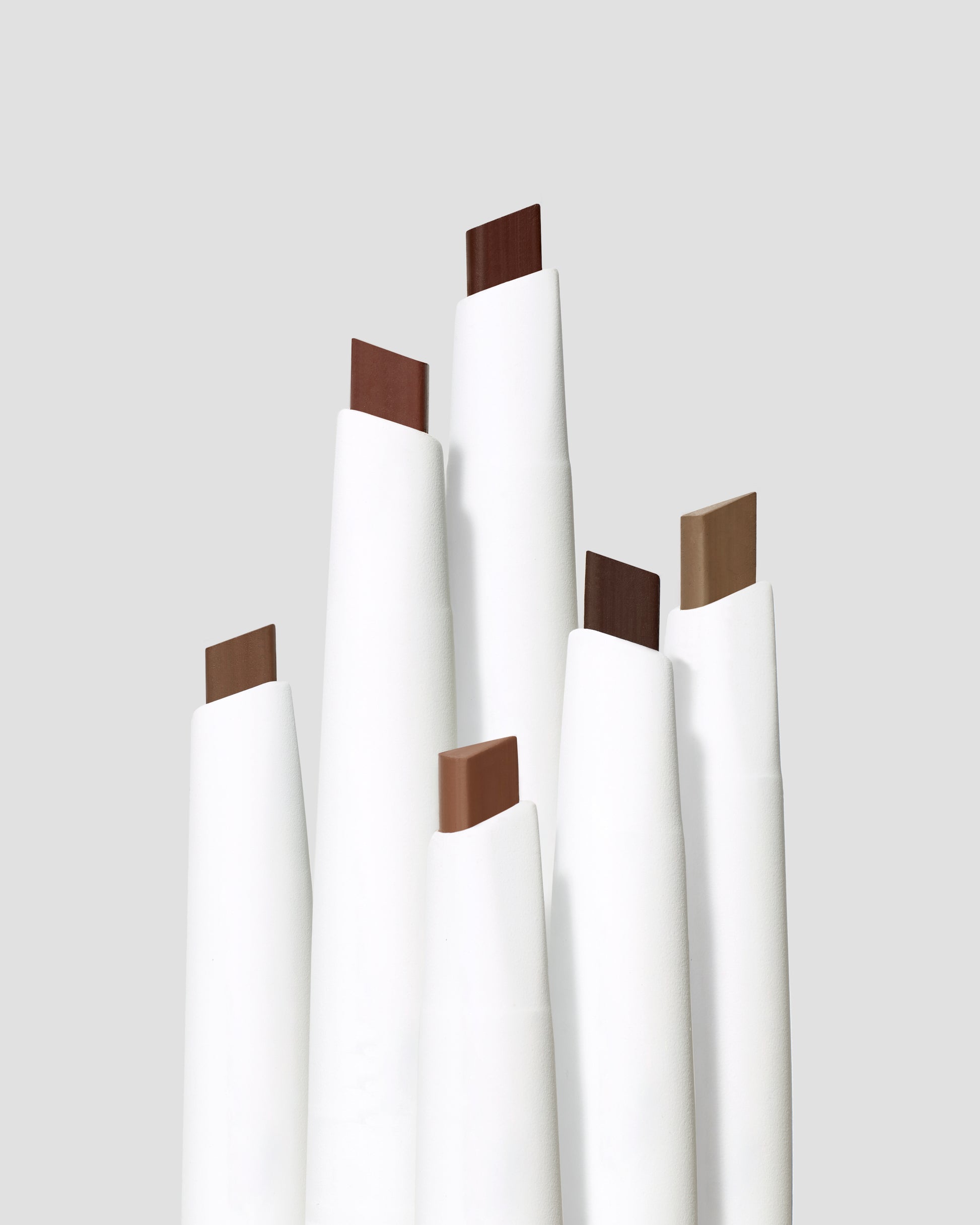 PureBrow® Shaping Pencil collection, six matte-white tubes showcasing different brow shades, featuring a built-in spoolie for precise, long-lasting brow definition.