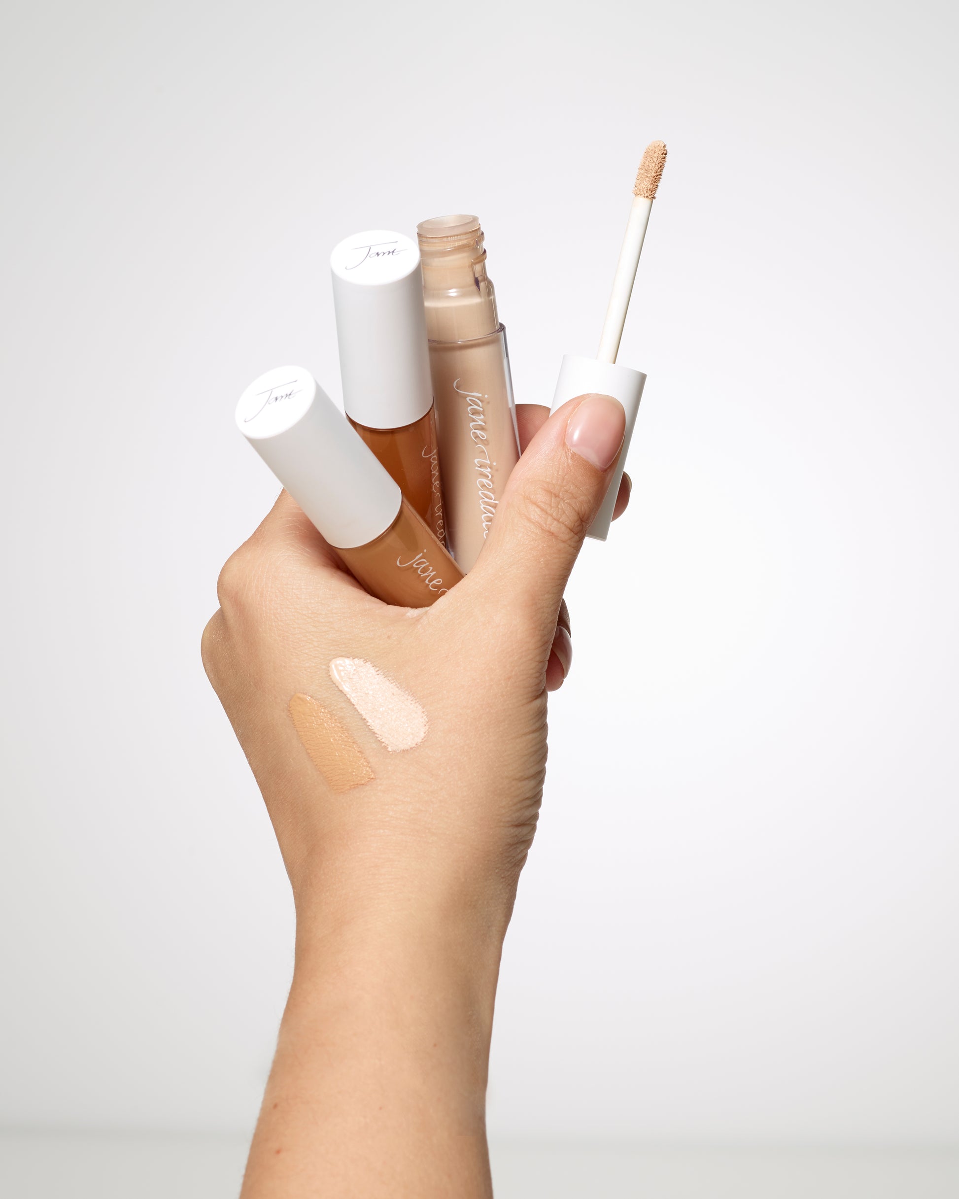 Hand holding PureMatch™ Liquid Concealer tubes, one open with wand, showing two skin-tone swatches; lightweight, buildable coverage for natural, seamless finish.