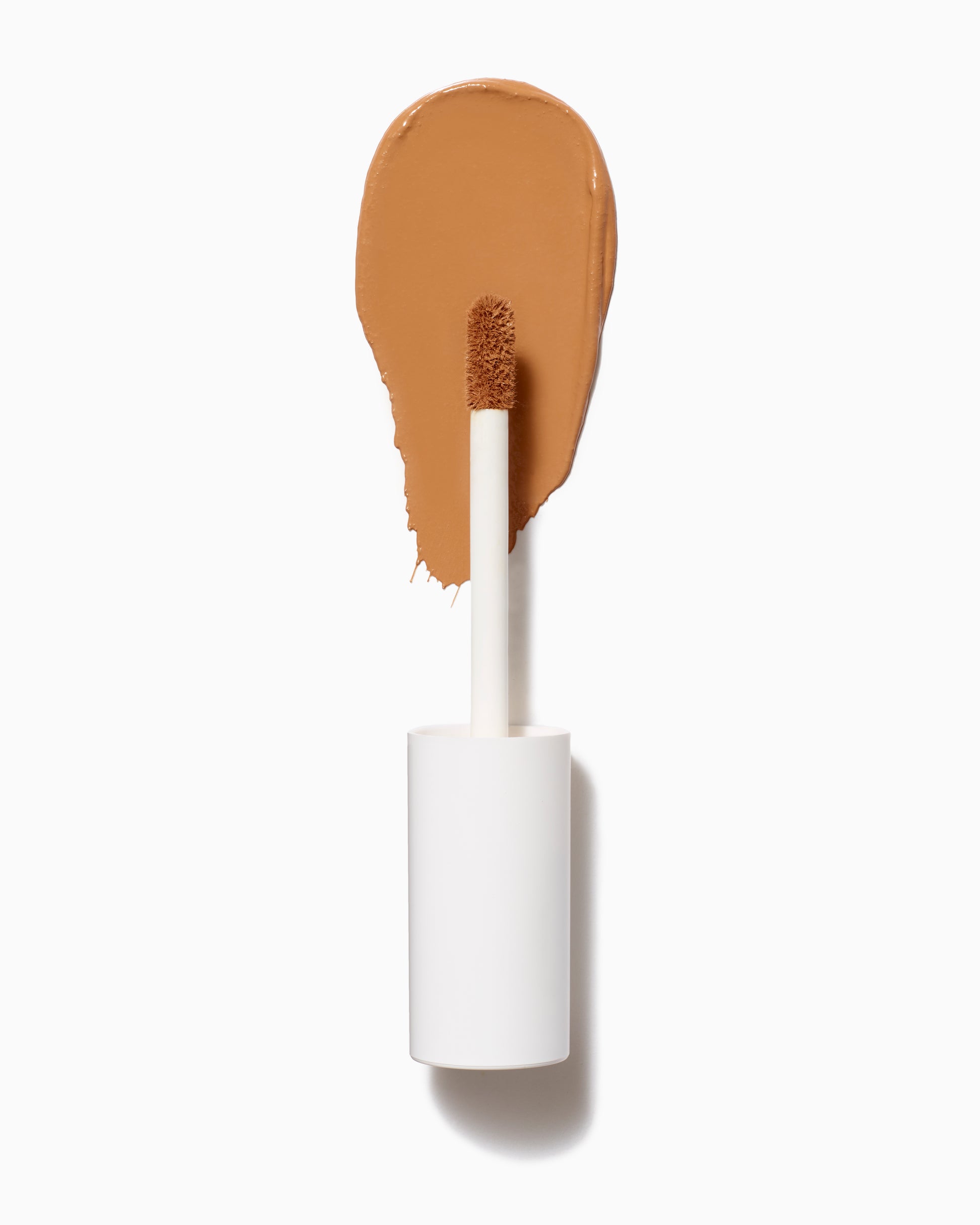 PureMatch™ Liquid Concealer with a white-handled doe-foot applicator, showcasing a warm tan cream swipe, highlighting its natural, buildable coverage and seamless blending capabilities.