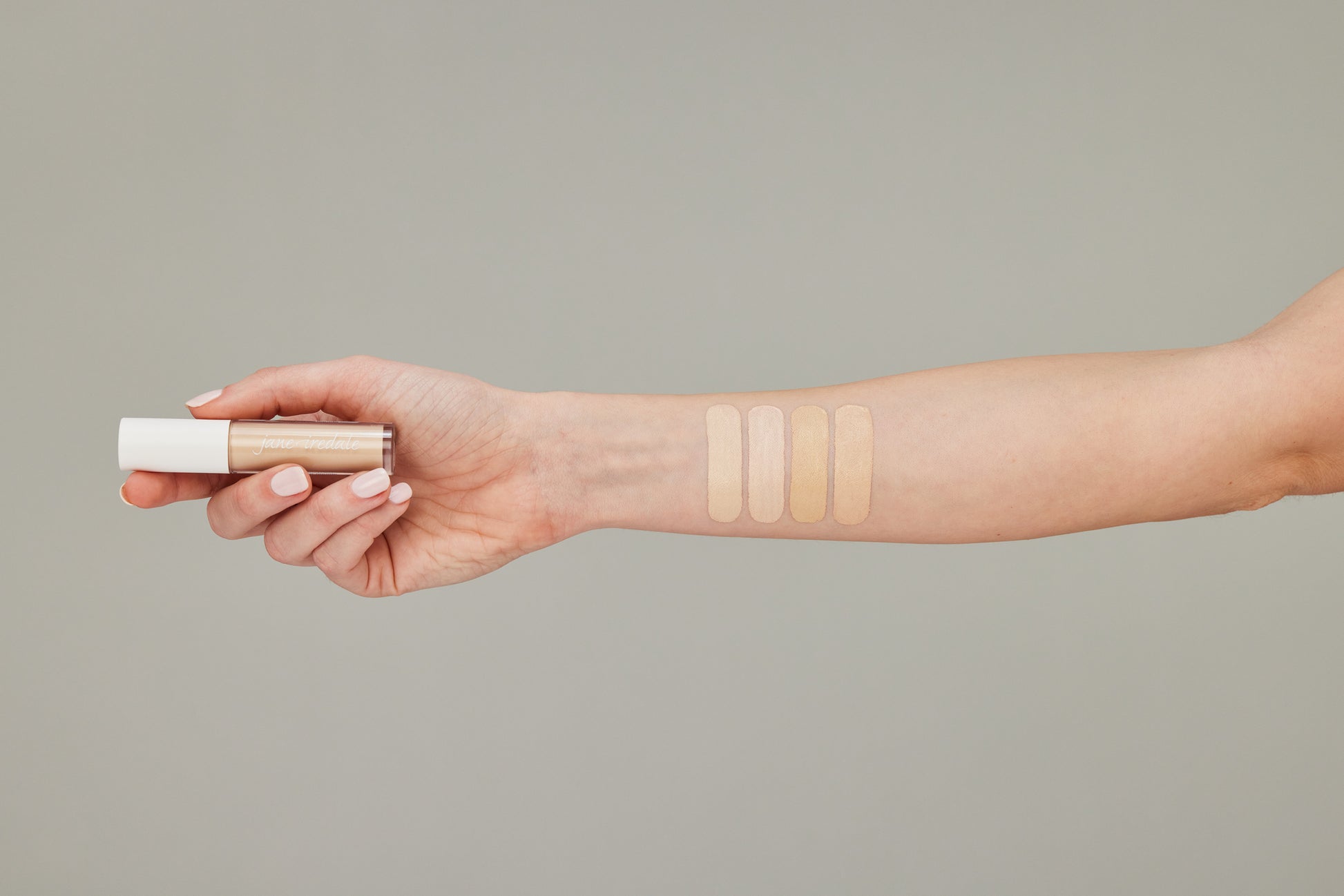 Forearm displaying four PureMatch™ Liquid Concealer shades, held tube emphasizes skin-like finish and buildable coverage, highlighting Beauty Shop Bellaire's inclusive, sustainable makeup range.