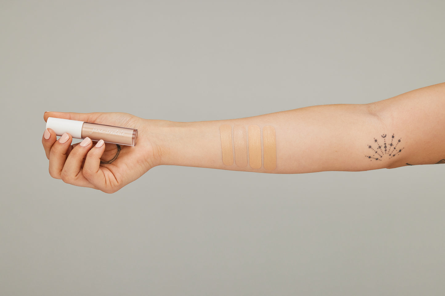 Forearm displaying four PureMatch™ Liquid Concealer swatches, showcasing diverse shades, held in hand with jane iredale tube, emphasizing blendable, natural finish.