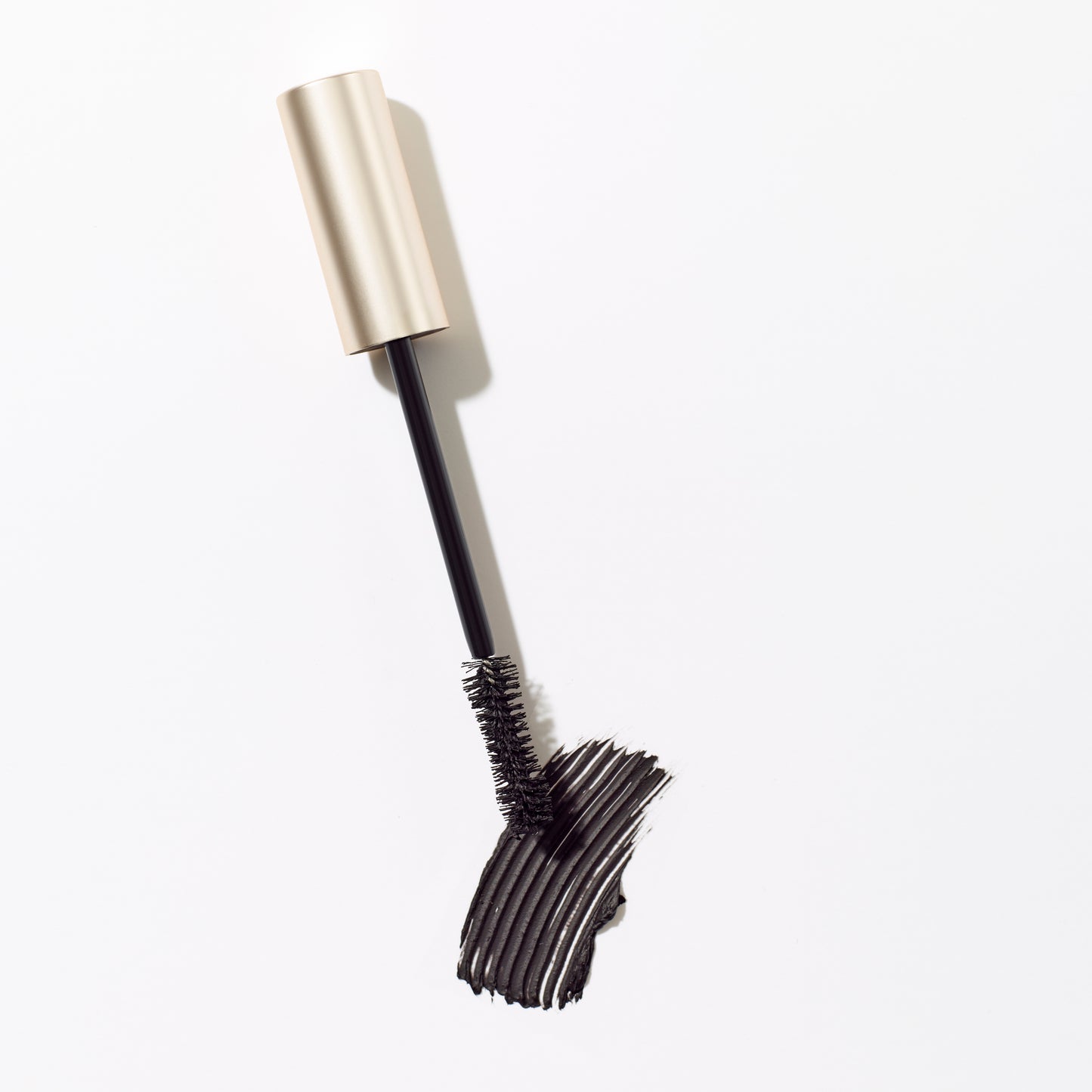 Beyond Lash™ Volumizing Mascara with gold-tone cap and spoolie brush on white background, showcasing a curved black mascara swatch for bold, nourishing volume.