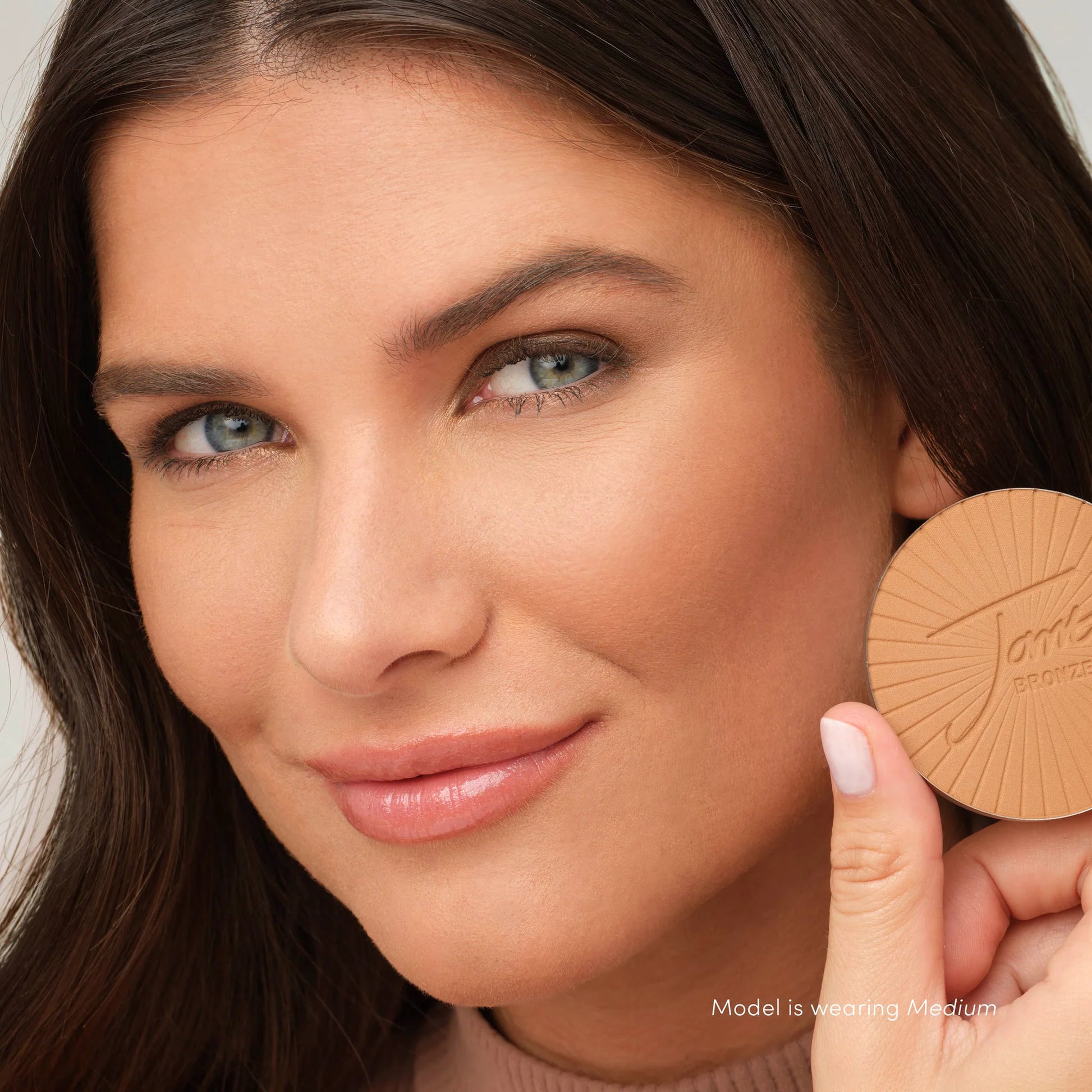 Close-up of woman holding PureBronze™ Matte Bronzer Powder Refill, showcasing its natural, weightless matte finish for contouring and sun-kissed skin. Available in Light, Medium, Dark.
