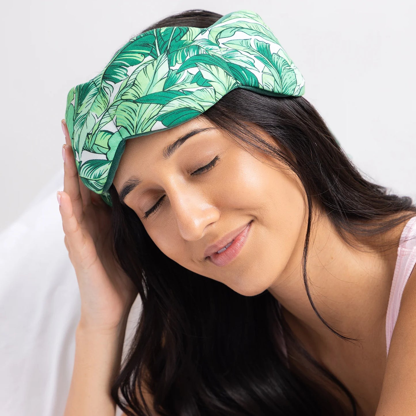 Young woman using The Weighted Blanket for your Eyes, a botanical-print eye mask by Nodpod, promoting relaxation and tension relief through even pressure distribution.