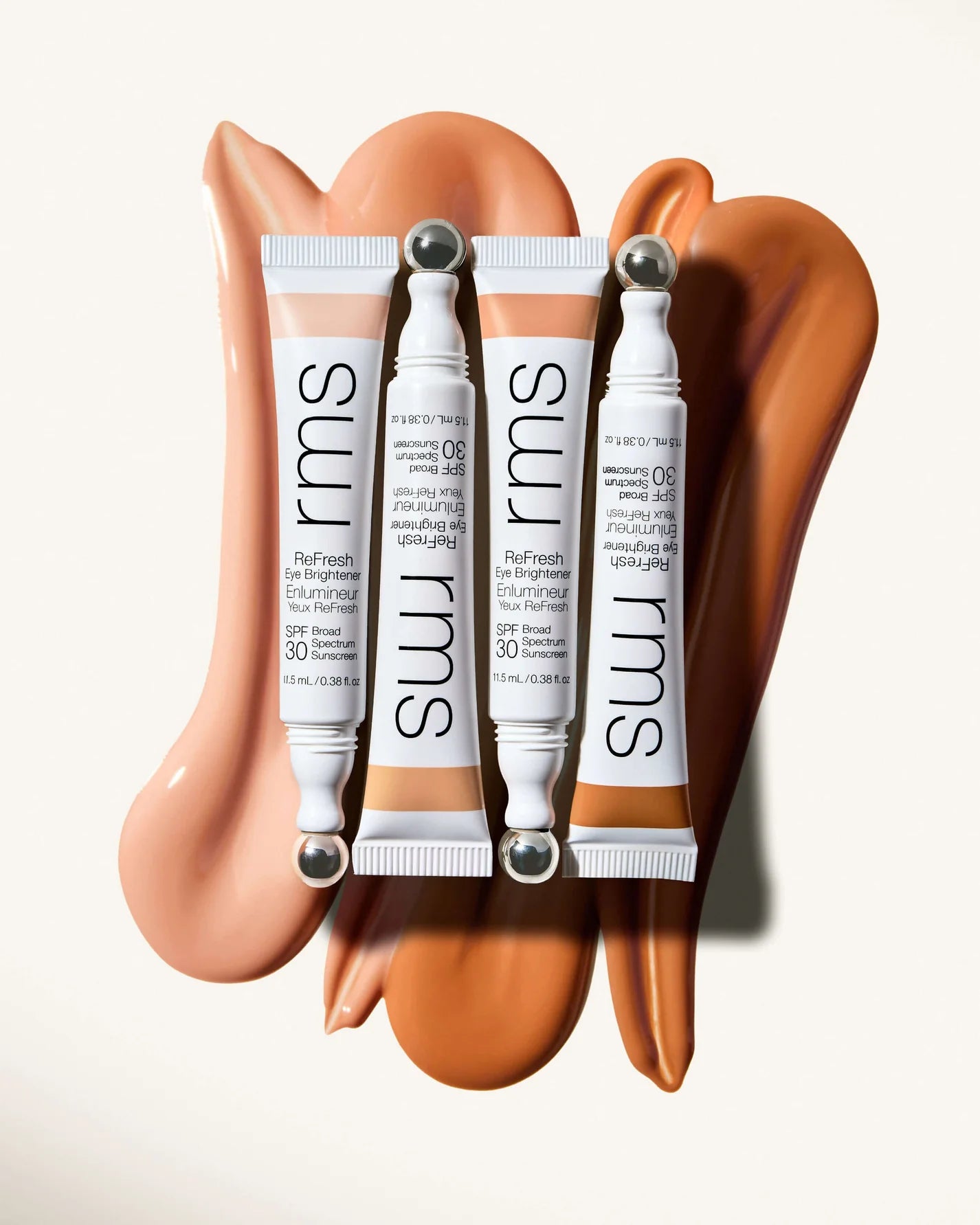 RMS Beauty's ReFresh Eye Brightener SPF 30 tubes with metal roller-ball applicators, displayed on product swatches for various skin tones.