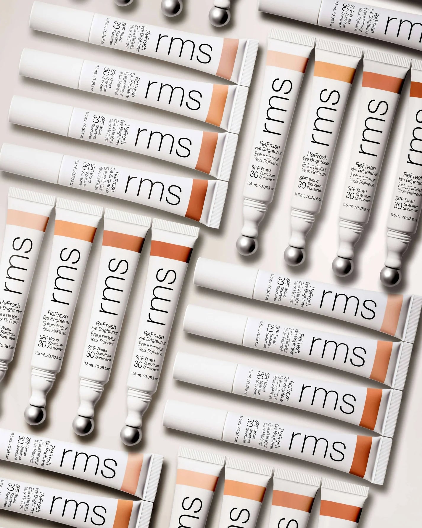 RMS Beauty's ReFresh Eye Brightener SPF 30 tubes arranged flat-lay; features metal-ball applicator, offering sun protection and undereye brightening in four shades.