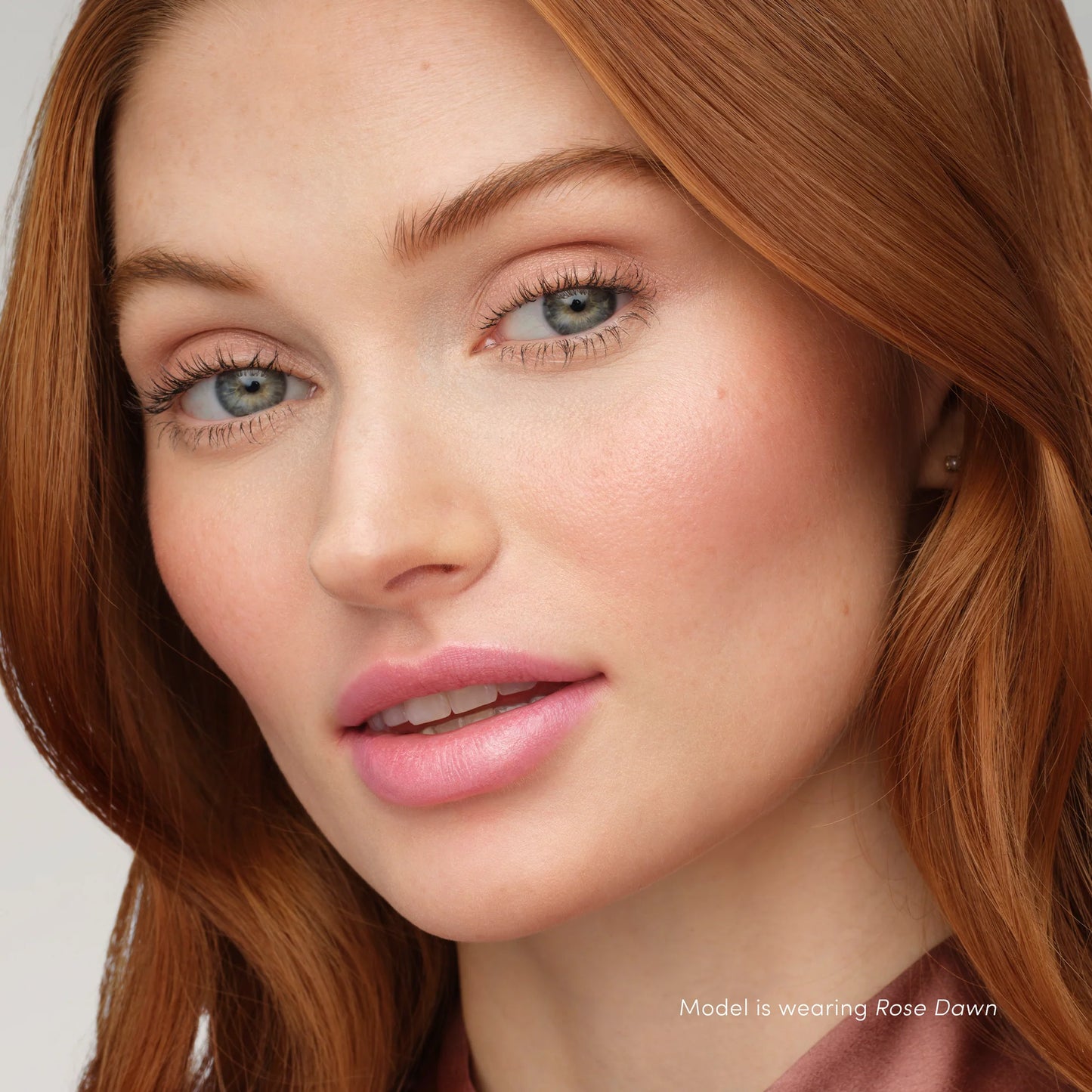 Woman wearing Rose Dawn makeup with copper-red hair, showcasing PureBronze™ Shimmer Bronzer Palette Refill's radiant, multipurpose shades for a glowing look.