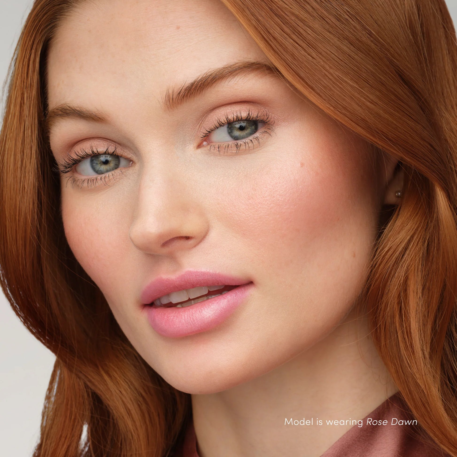 Woman wearing Rose Dawn makeup with copper-red hair, showcasing PureBronze™ Shimmer Bronzer Palette Refill's radiant, multipurpose shades for a glowing look.