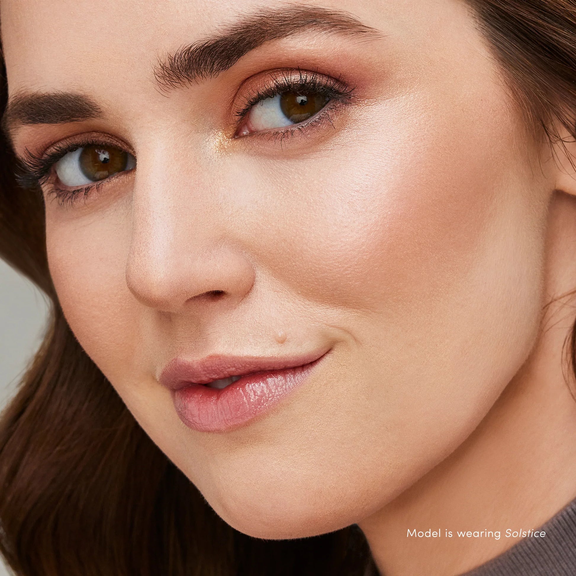 Young woman wearing warm shimmery makeup with Glow Time® Highlighter Stick in Solstice, highlighting cheekbones for a natural, radiant glow.