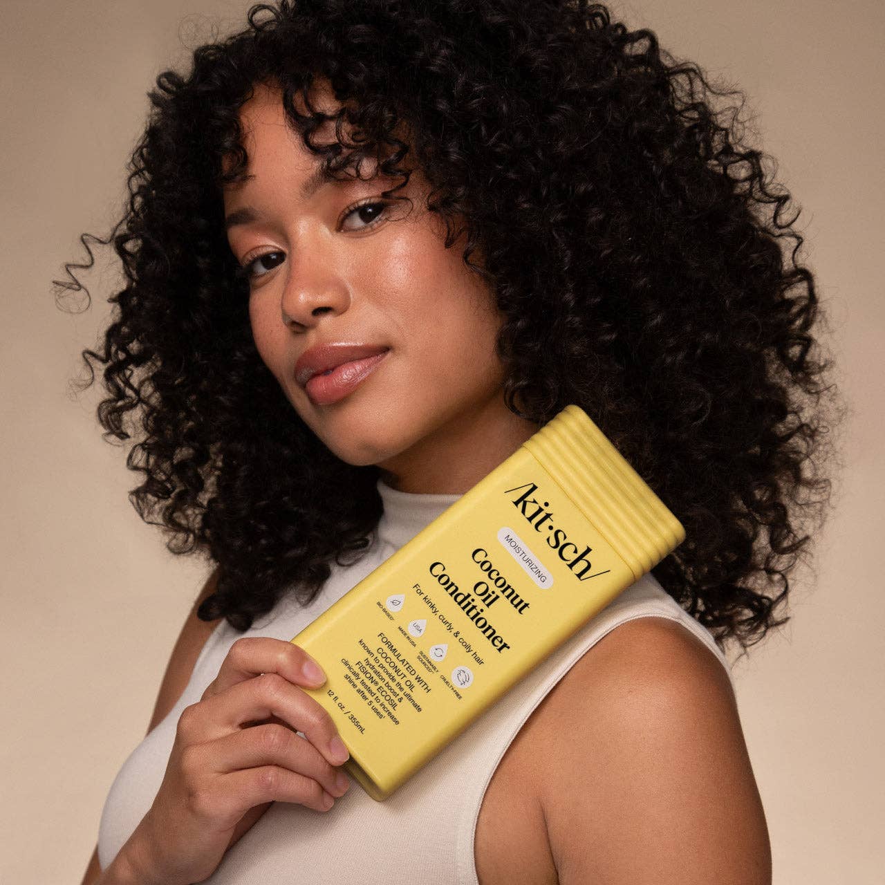 Young person with curly hair holds a Moisturizing Coconut Oil Conditioner bottle, formulated for curly hair, featuring coconut oil and panthenol for hydration and shine.