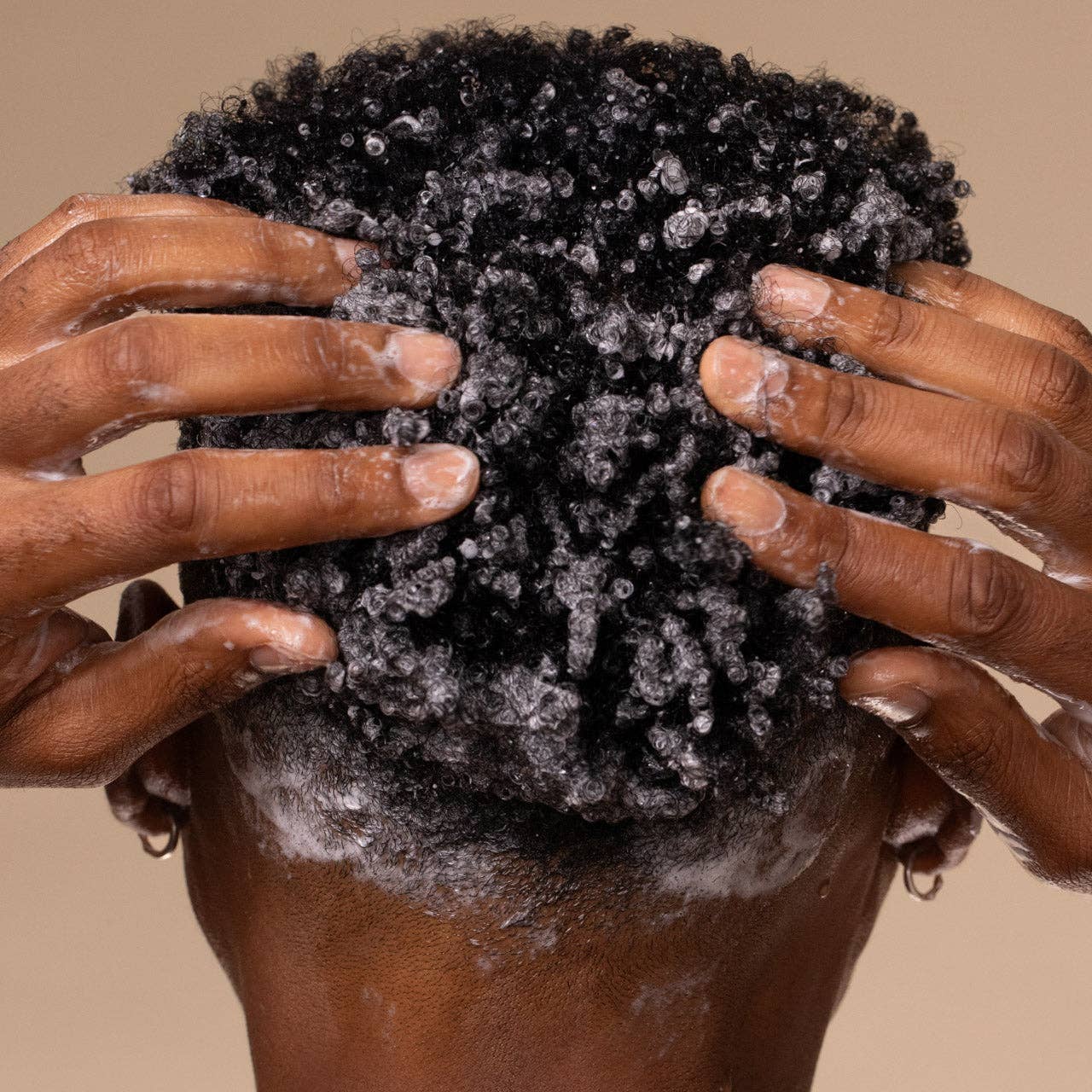 Person with afro-textured hair lathered in Moisturizing Coconut Oil Shampoo, hands massaging suds into scalp, highlighting product's hydrating and cleansing benefits for curly hair.
