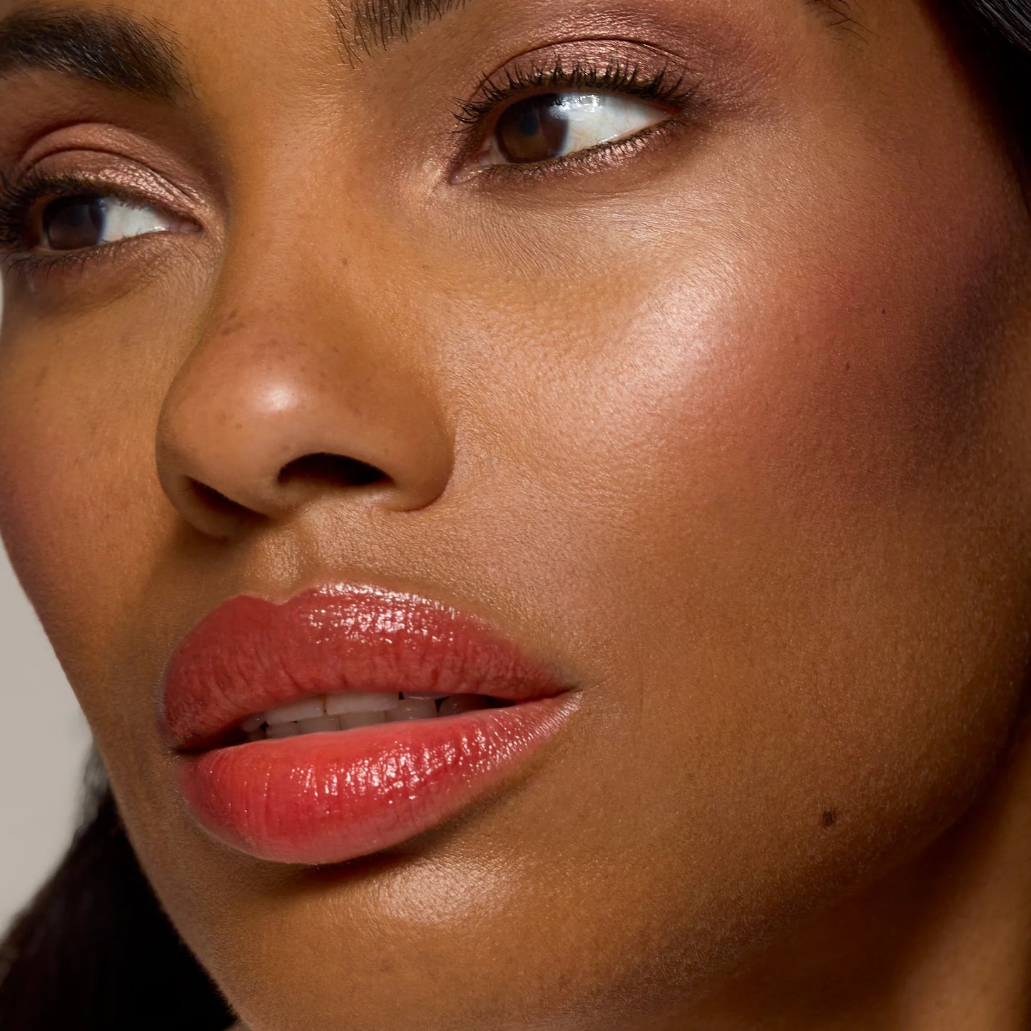 Close-up of a woman's face showcasing Glow Time® Bronzer Stick, highlighting her sun-kissed glow with smooth skin, glossy lipstick, and shimmering eyeshadow.