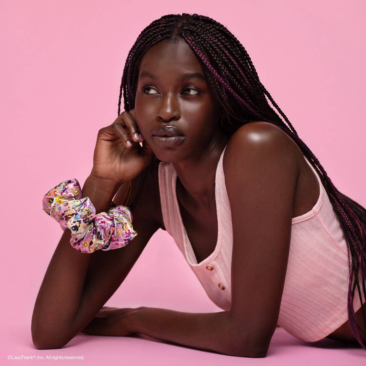 Young woman with braids wears Lisa Frank x Kitsch Pillow Scrunchie® on wrist, showcasing its colorful, satin texture ideal for gentle hair care.