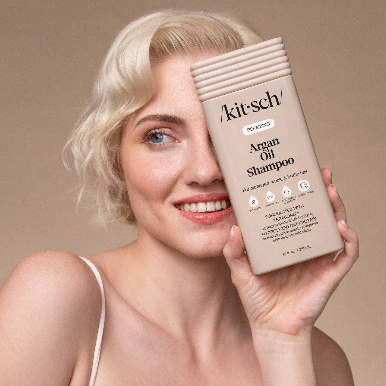Woman holding Kitsch Repairing Argan Oil Shampoo bottle, showcasing bio-based, cruelty-free, sustainably sourced formula for damaged hair with Terabond™ and Hydrolyzed Oat Protein benefits.