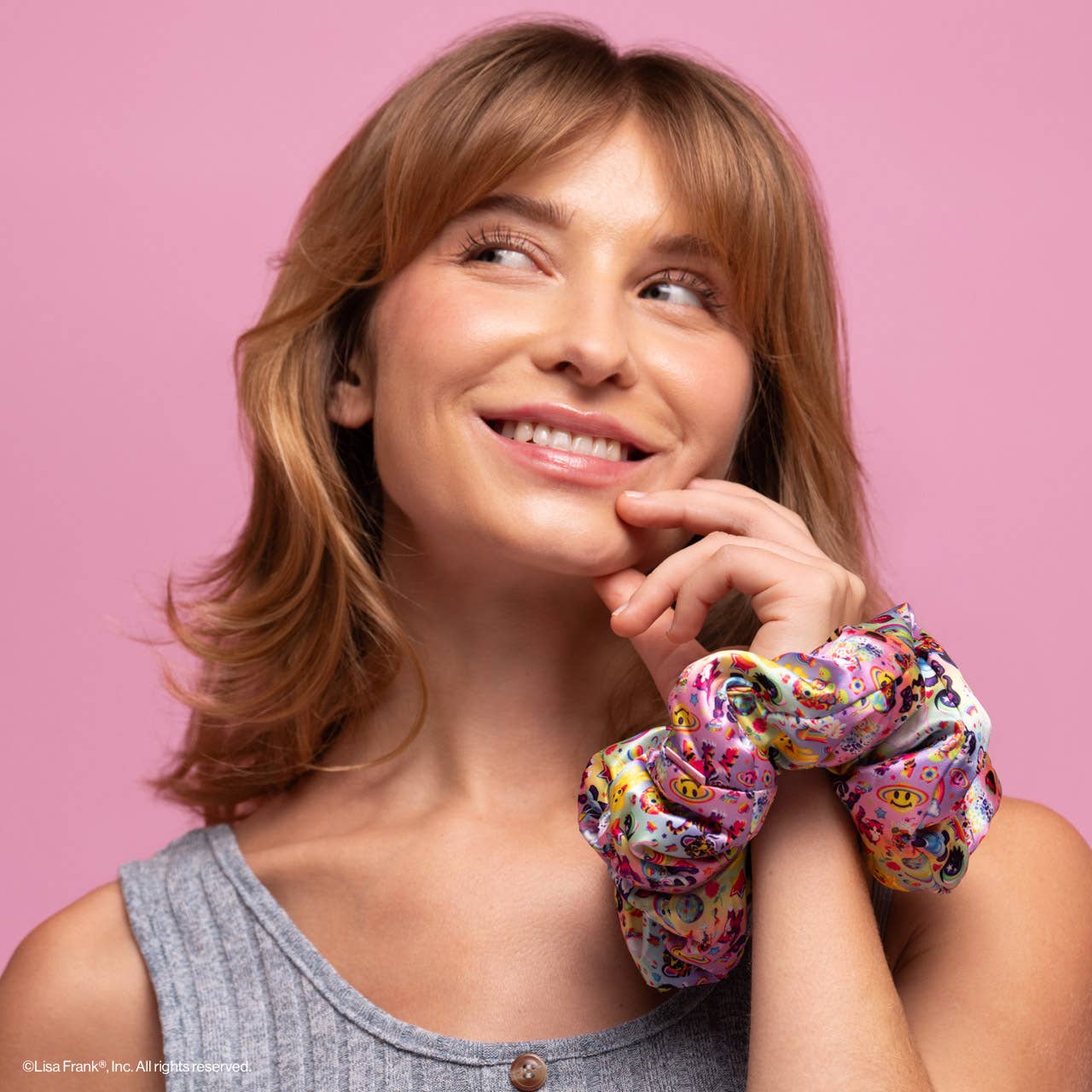 Young woman with playful smile wears Lisa Frank x Kitsch Pillow Scrunchies® in Satin, featuring colorful, whimsical designs, highlighting their vibrant, protective hair styling appeal.