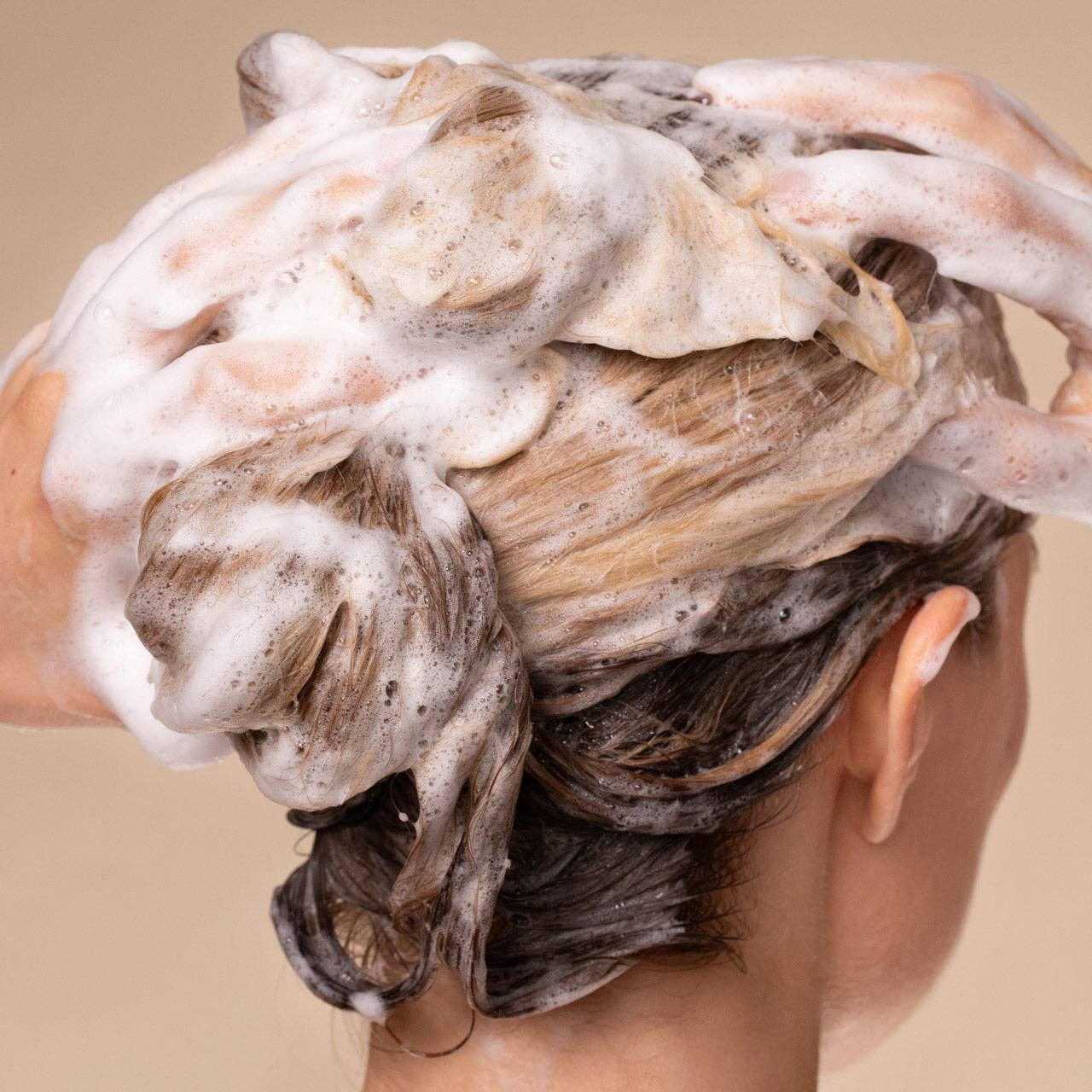 Hands massaging shampoo into hair, creating suds, illustrating the Strengthening Rice Water Shampoo's volumizing and shine-boosting effects for thin, fine, damaged hair.